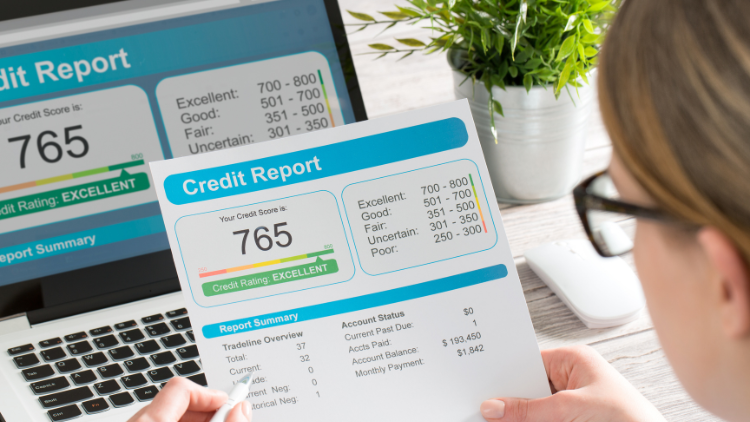 A woman wearing glasses looks at her credit report digitally and in print showing an excellent rating with a score of 765.