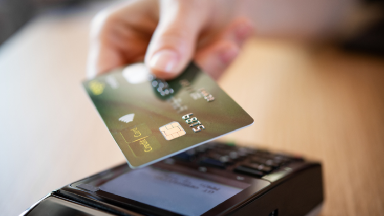 A person holds a credit card above a payment terminal to make a contactless purchase.