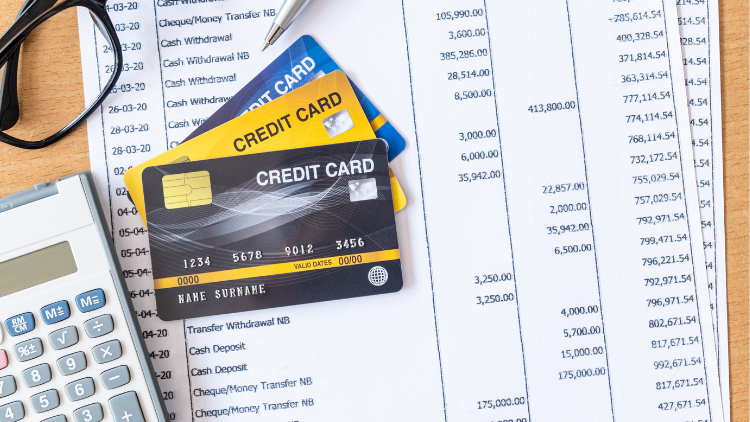 Several credit cards rest on top of a financial statement with a calculator and pen, highlighting monthly spending analysis.