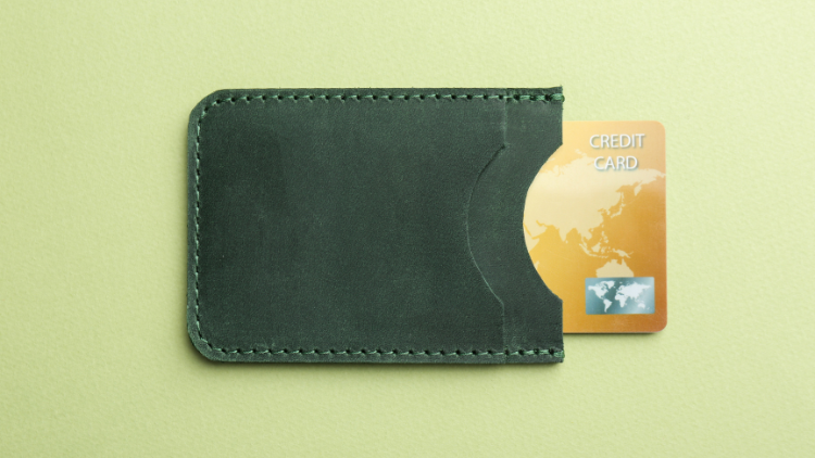 Gold credit card partially tucked into a dark green leather wallet against a plain background.