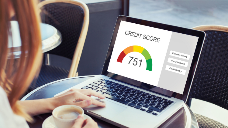 A person at a café holds a coffee while using a laptop displaying a credit score dashboard with a colorful gauge showing 751 and categories like Payment History, Amounts Owed, and Credit History.