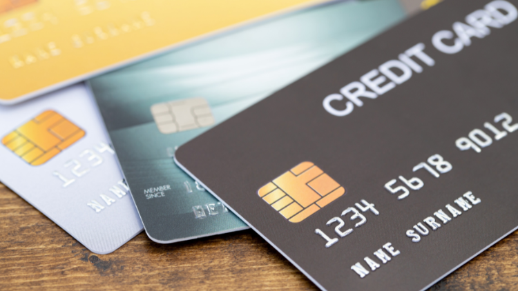 A close-up of multiple credit cards in different colors arranged in a neat stack on a wooden surface.