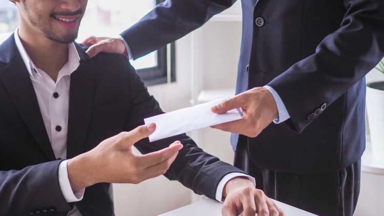 Businessman happily receiving an envelope of cash bonus from a colleague in an office setting.