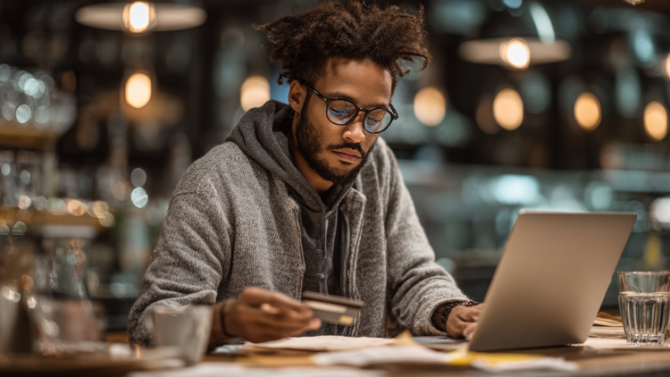 A young entrepreneur works on a laptop while holding a credit card, illustrating the use of starter business credit cards to build credit history.