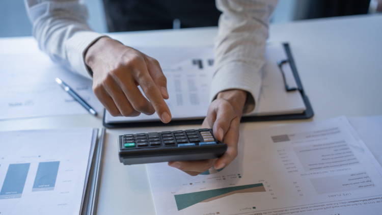A person points at a calculator while reviewing graphs and documents related to financial planning.