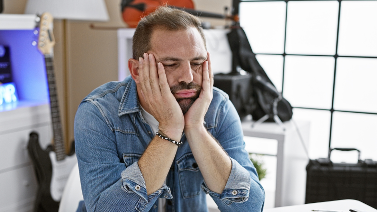 Man sitting at a desk with his hands on his face looking stressed about financial problems.