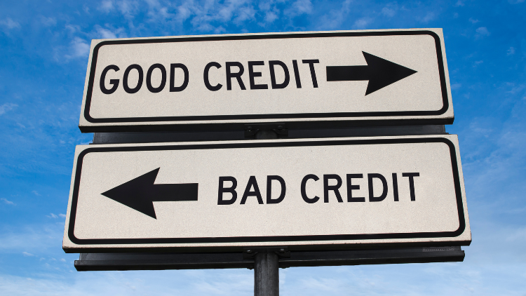A road sign with arrows pointing in opposite directions for good credit and bad credit under a clear blue sky.