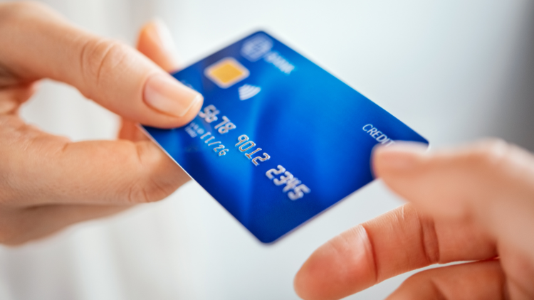 A close-up view shows a person holding a blue credit card between their hands, ready for payment.