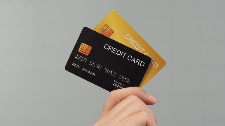 Person holding two credit cards, one black and one gold, between their fingers.