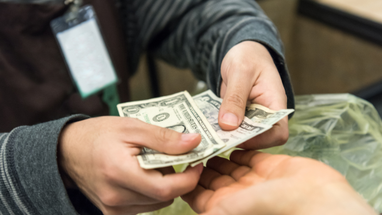 A person hands over several U.S. dollar bills to another individual during a transaction.
