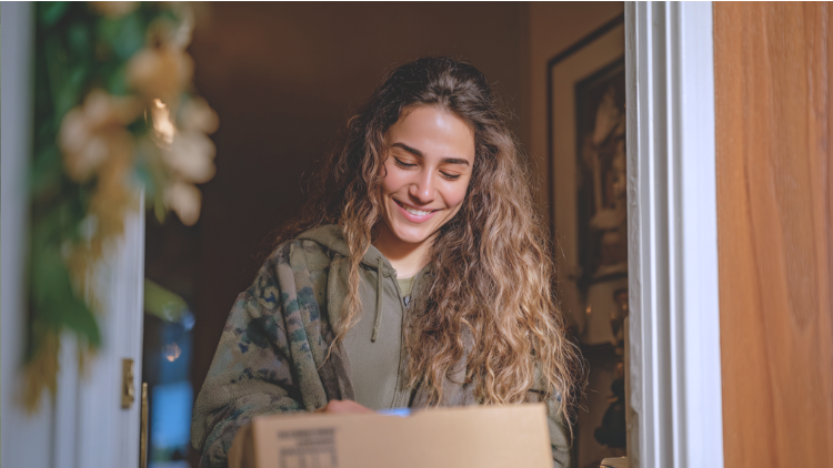 A smiling woman receives a package delivery at her front door.