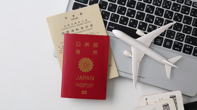 A red Japan passport and international travel documents rest on a laptop keyboard beside a small airplane model.