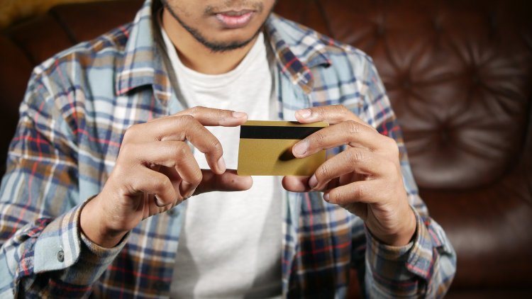 A man in a plaid shirt examines a gold credit card while seated on a leather couch.