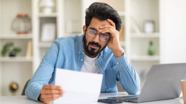 A worried man reading overdue bill at home office.