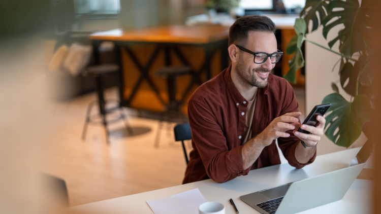 Smiling man at his desk using a mobile phone to link dining apps and earn bonus points from restaurant purchases.