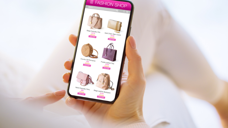 A shopper browses handbags on an online fashion store using a smartphone.