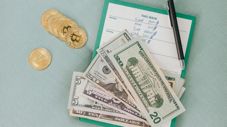 US dollar bills and bitcoin coins placed on a weekly budget planner with handwritten expenses.