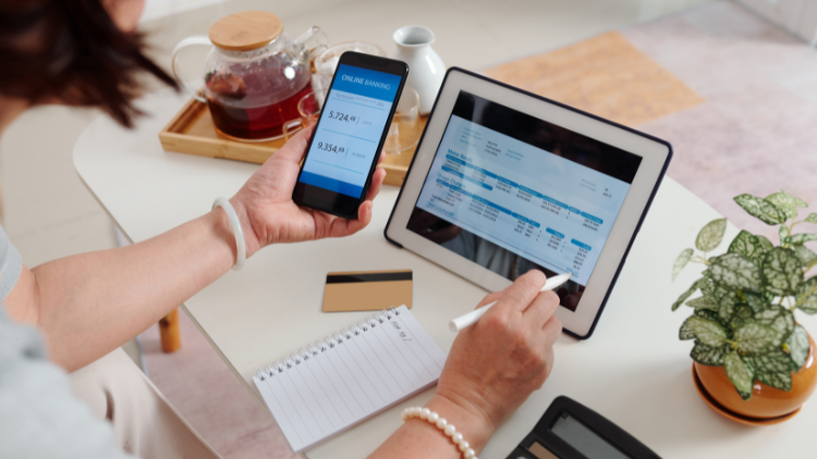 A person uses a smartphone and tablet to check online banking balances and track financial transactions.