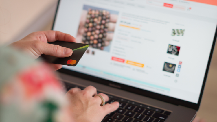 Smiling man sitting on a couch holding a credit card while shopping online with his laptop.