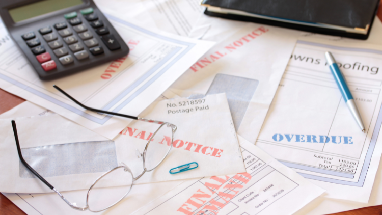 Overdue bills and final notice letters with calculator and glasses on desk.