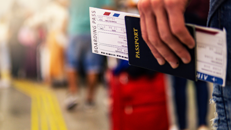 A traveler holds a passport and boarding pass while standing in line at the airport.