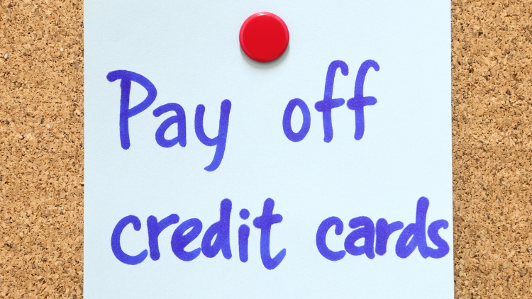 A handwritten note pinned to a corkboard reminds to pay off credit cards.