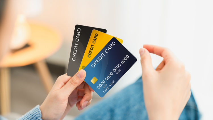 A person’s hands holding three different colored credit cards while sitting casually, suggesting card choice options.