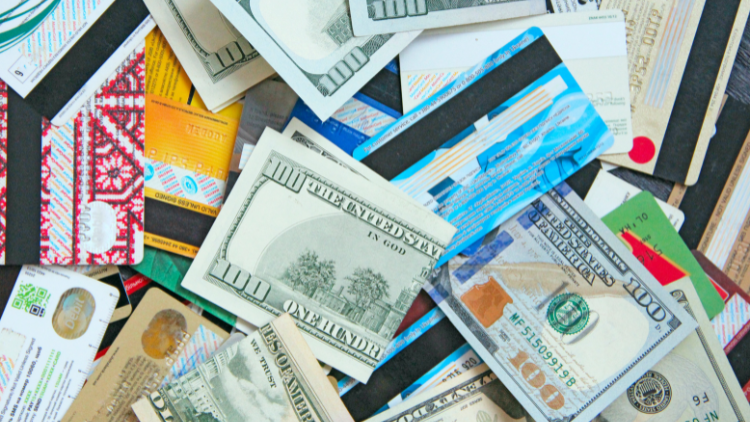 A messy pile of various credit cards and hundred-dollar bills is spread across a surface.