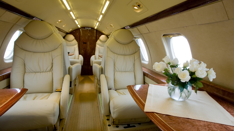 The cabin of a private jet features plush leather seats and a table decorated with fresh white roses.