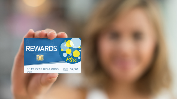 A woman holds a blue Rewards Plus credit card close to the camera, highlighting its chip and bold design.