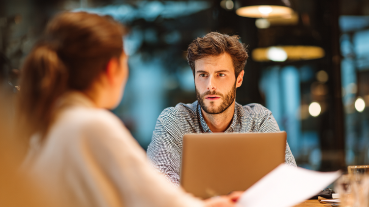 A man listens intently to a colleague during a financial discussion in an office setting.
