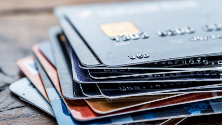 A close-up of several stacked credit cards placed on a wooden surface, symbolizing financial tools for business expenses.