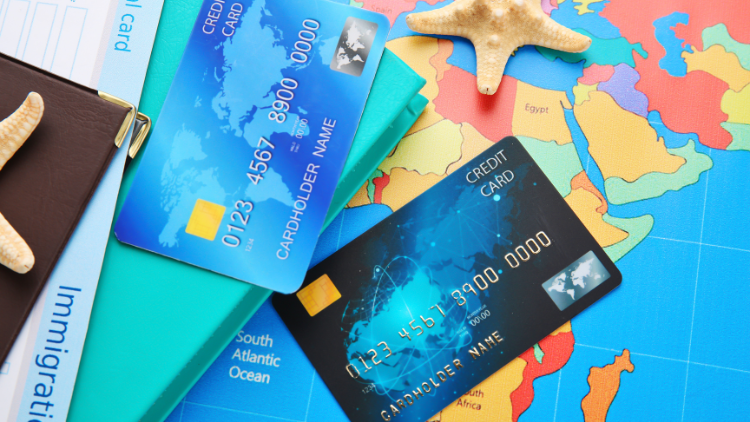 Two credit cards placed on a colorful world map beside travel documents and starfish, symbolizing international travel.
