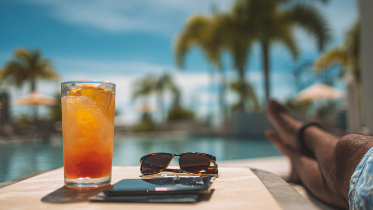 A refreshing tropical cocktail with orange garnish placed on a lounge chair by a poolside.