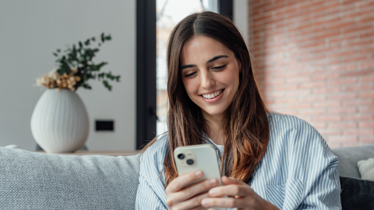 A cheerful woman sits on a couch and shops online using her smartphone.